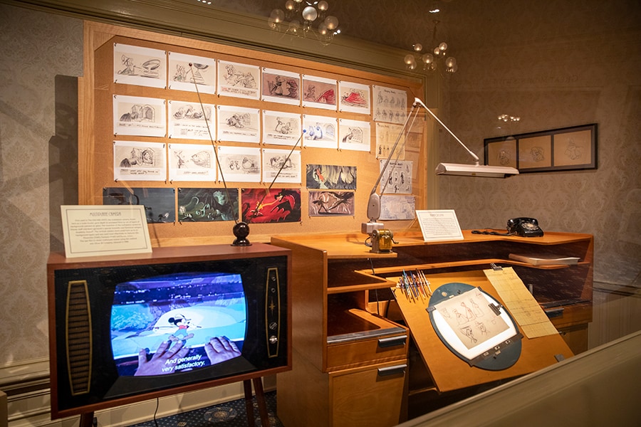A recreated animator's room including a desk, drawings and a television set playing a featurette