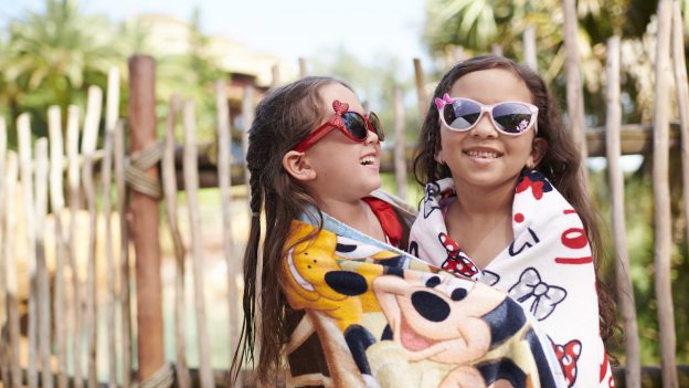 Kids by a pool wrapped in a Disney towel with Disney sunglasses on