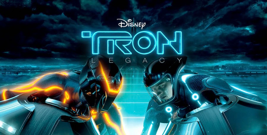 Two Lightcycles battle on the Grid with one program named CLU shown in orange and the other, Sam Flynn, is shown in blue. The two are leaning in toward each other with the “TRON: Legacy” logo in the background