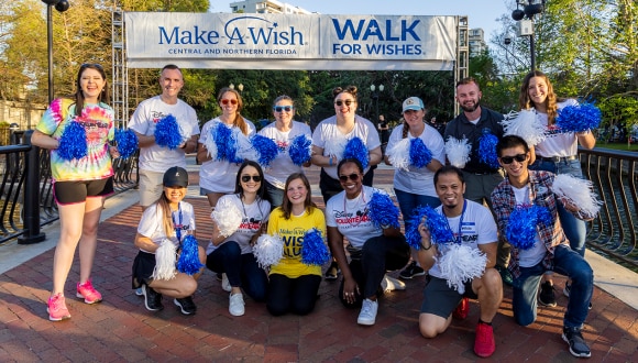 Disney VoluntEARS smile together while holding pom moms in front of a Walk for Wishes banner.