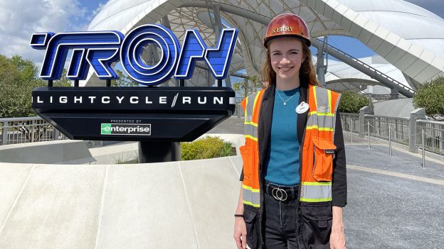 Kerry stands in her Imagineer vest and helmet in front of the TRON / Lightcycle Run sign at the entrance to the concourse.