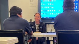A cast member seated at a conference table between two program participants
