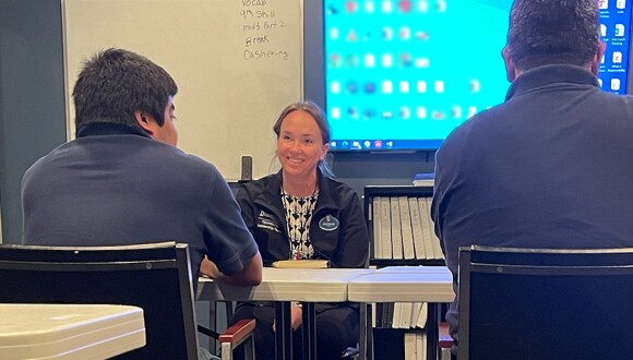 A cast member seated at a conference table between two program participants