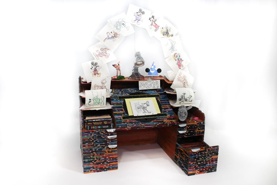 An animator's desk constructed from recycled art pencils, with drawings of Mickey Mouse flying in an arc above it