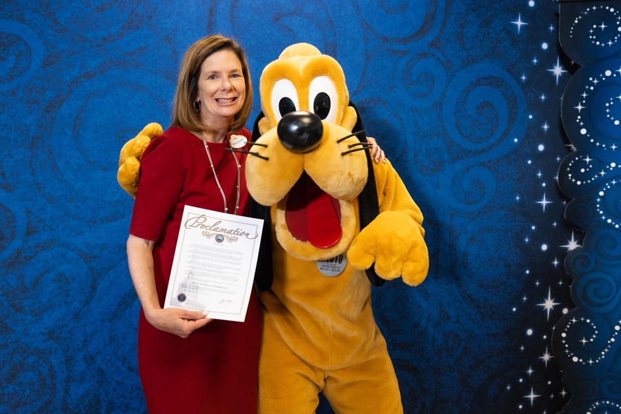 Cast member with Pluto while holding letter from Tampa Mayor proclaiming May 11 a Celebrate Disney Cast Members Day