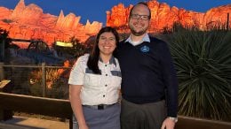 Cast members Brianna and James standing in front of Radiator Springs Racers at dusk