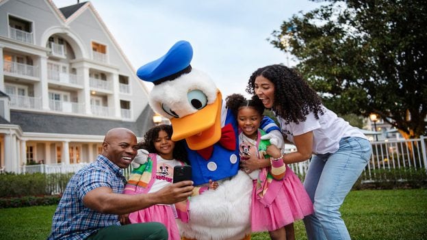 family of 4 people hugging Donald Duck in front of a house taking a selfie