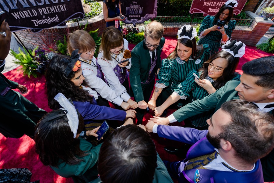Haunted Mansion cast from around the world standing on the red carpet, putting their hands into a circle