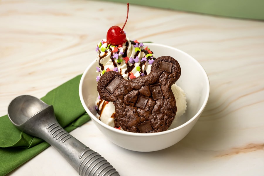 Mickey Shaped brownie, hot fudge, whipped cream, Mickey-shaped sprinkles, and a cherry on top on a bowl next to an ice cream scooper from Hollywood Scoops at Disney's Hollywood Studios 