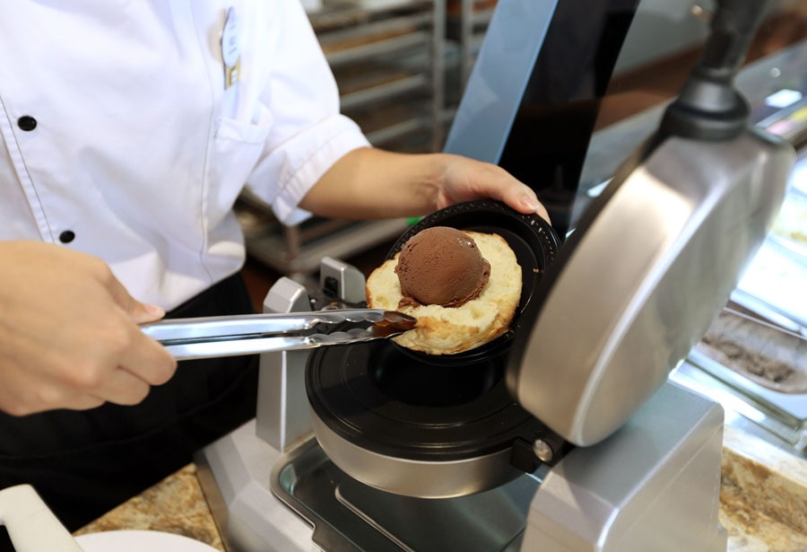 A person at EPCOT making a Croque Glacé that has a scoop of ice cream pressed in brioche bun