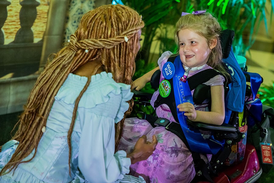 Young female wish child in a wheelchair smiles at live action Ariel.