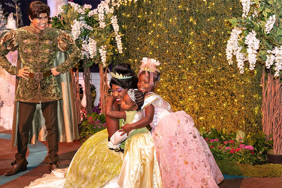 Two young girls hug Tiana with Naveen watching nearby. 