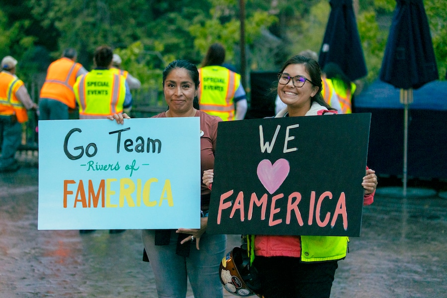 Two cast members holding signs cheering on the Rivers of FAMerica team