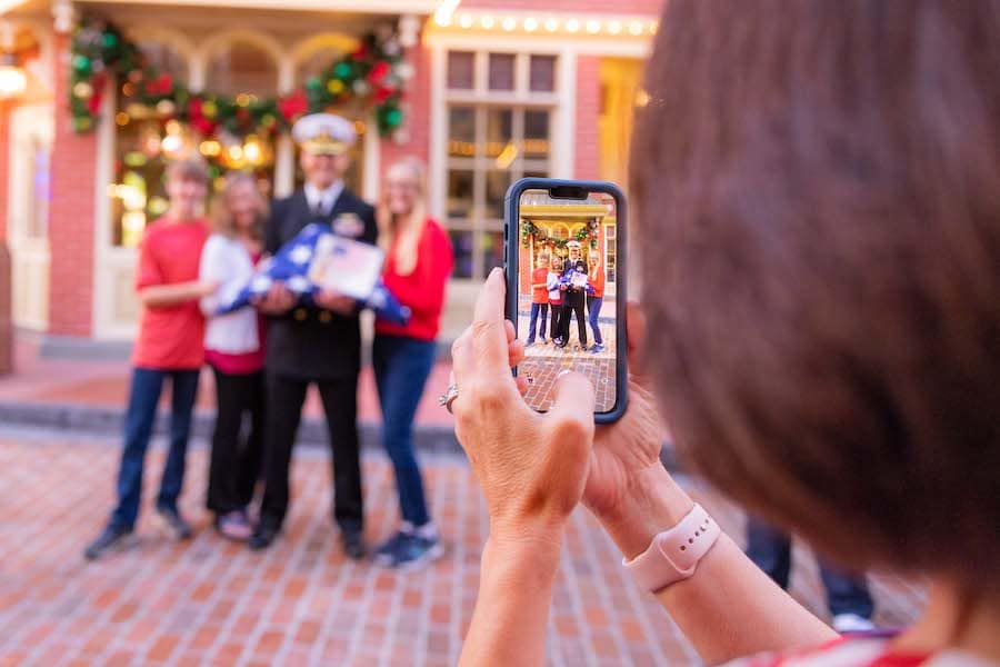 A Family Member takes photo of U.S. Navy Officer and Veteran Cast Member during a Flag Retreat Ceremony in Magic Kingdom Park