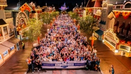 A large group of cast members gathered at nighttime on Main Street, U.S.A. behind a banner reading "Thank You for 100 Years"