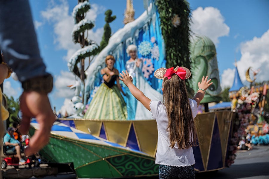 A kid waving to Anna and Elsa in a parade at Magic Kingdom Park at Walt Disney World Resort