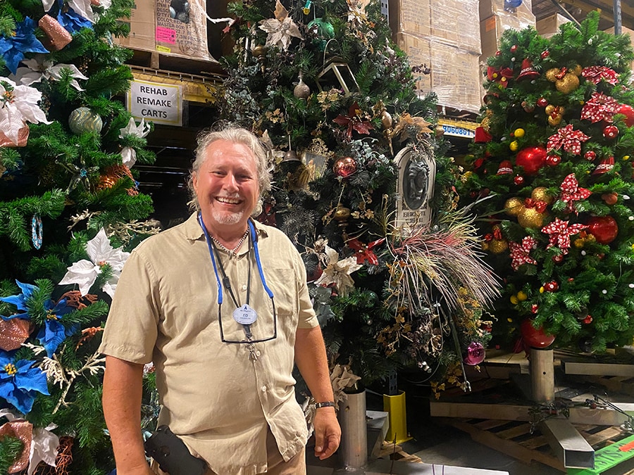 Ed smiles in front of some Disney Springs trees in progress in the Holiday Services warehouse. 