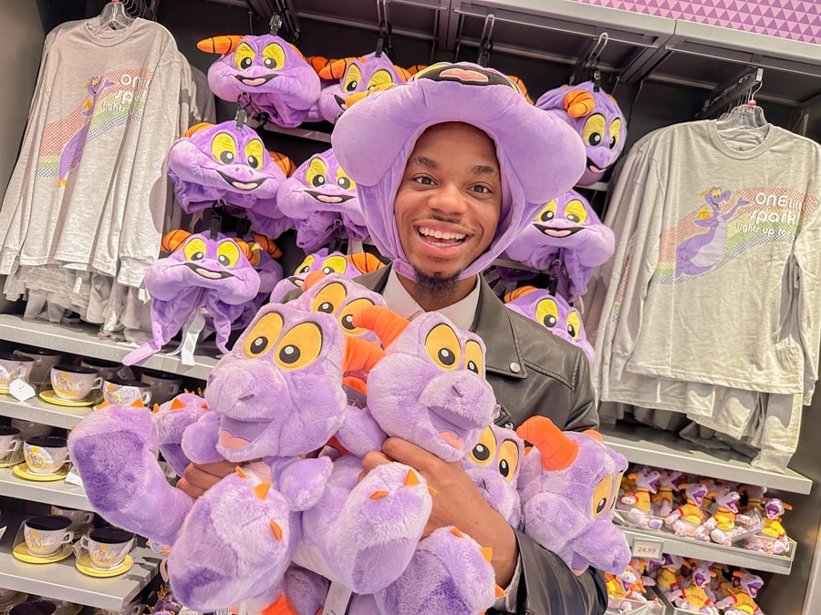 Image of guest wearing Figment plush hat and holding Figment plush with additional Figment merch in the background