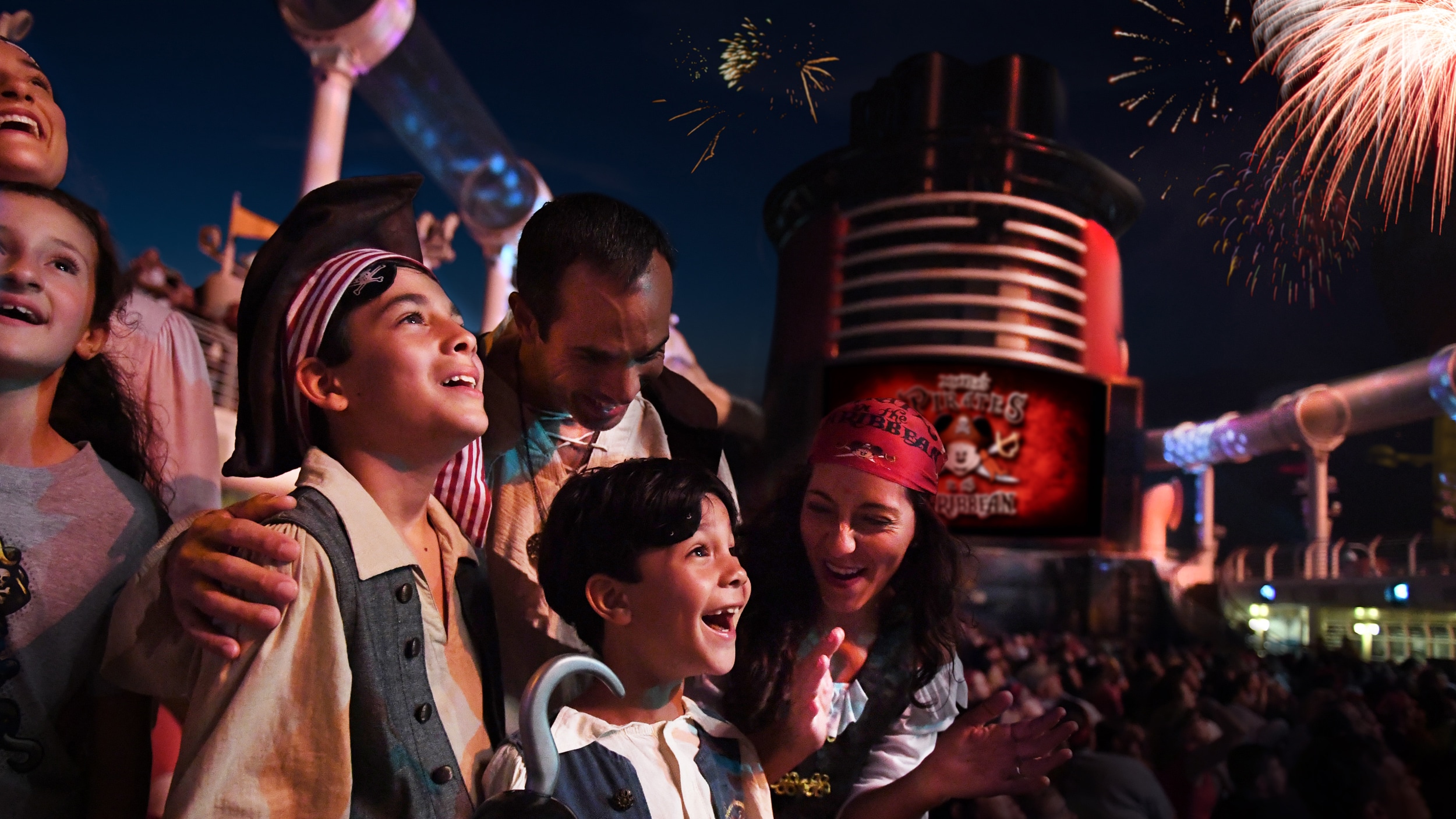 Vestidos de piratas, una familia se maravilla ante los fuegos artificiales durante una fiesta en cubierta de un crucero de Disney Cruise Line