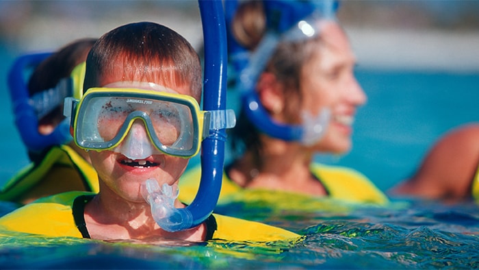 Un jeune visiteur dans l'eau, portant un masque, un tuba et un gilet de sauvetage
