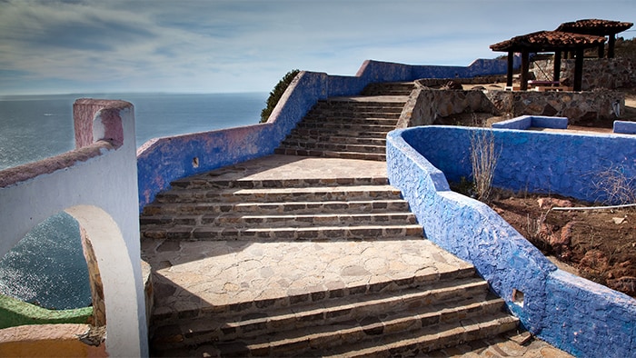 Uma escadaria de pedra, com patamares a cada cinco degraus, leva ao mirante com vistas litorâneas.