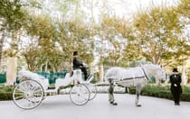 Two coachmen in tuxedos with gloves and top hats and a horse drawn carriage parked in a courtyard