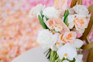 A bridal bouquet of roses, orchids and trailing greenery resting on a ceremony chair