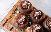 A plate of mini chocolate cakes with frosting and chocolate shavings