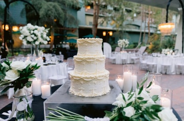 A 3 tier wedding cake with lace piping at an outdoor candlelit reception