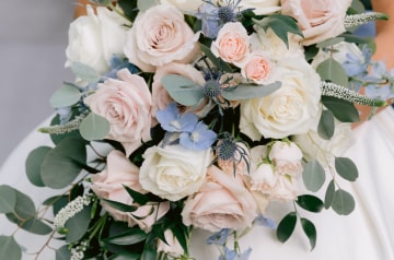 A bride in an off the shoulder gown holding a cascading bouquet of roses and wildflowers