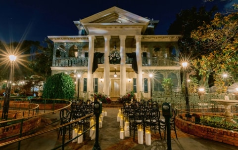 The Haunted Mansion with columns and ornate balconies illuminated for an evening wedding ceremony with candles