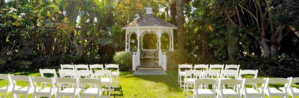 Rows of folding chairs and a gazebo on a lawn surrounded by trees