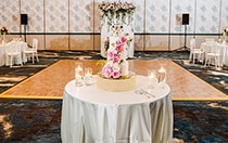 A cake decorated with several large roses on a table in the middle of a room also featuring a dance floor