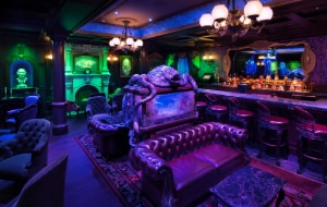The Haunted Mansion Parlor featuring spooky décor, a tank with skeletal fish and a mirror above the bar with hitchhiking ghosts