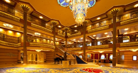 The Atrium in the Disney Dream featuring a staircase, chandelier, grand piano and statue of Captain Donald Duck