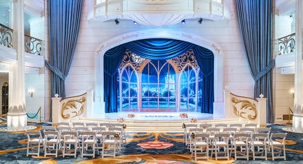 A lavish atrium set for a wedding ceremony aboard a Disney cruise ship with rows of chairs and floral arrangements flanking an aisle