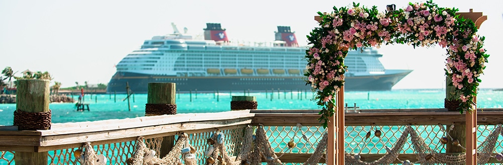 An archway covered in flowers overlooks the water and a Disney Cruise Line ship