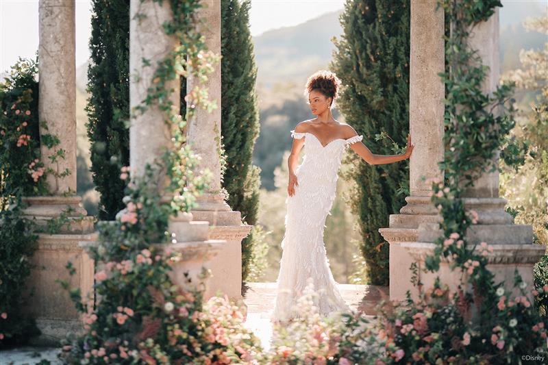 A woman in a wedding dress standing between vine covered stone columns in a lush outdoor setting