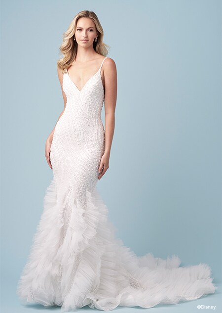 A bride wearing an Ariel inspired trumpet wedding gown featuring beading, a V neckline and a ruffled train