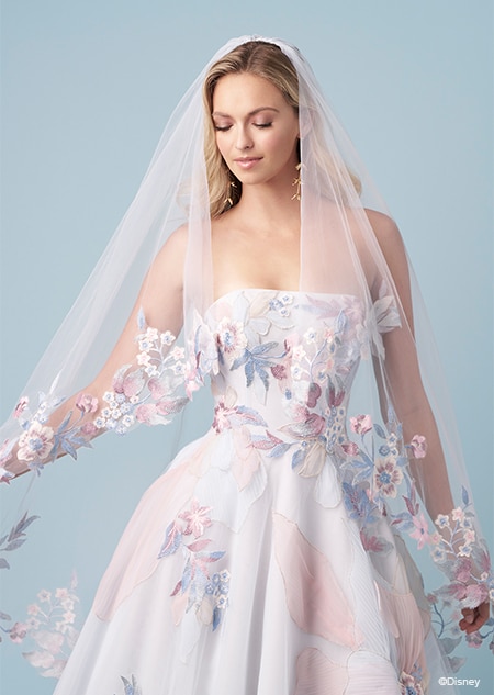 A bride wearing a veil and a strapless Rapunzel inspired A line wedding gown featuring a straight across neckline and large embroidered flowers