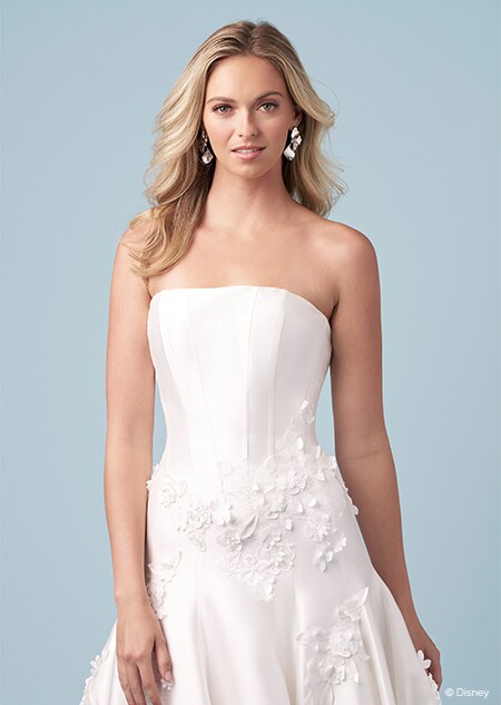 A bride wearing a strapless Aurora inspired A line gown with embroidered flowers and a straight across neckline