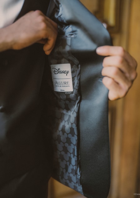 A man in a black tuxedo opening his jacket to reveal a Mickey Mouse patterned lining