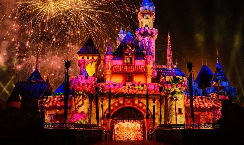 Fireworks bursting over Sleeping Beauty Castle which is illuminated to appear as Casa Madrigal from Encanto