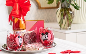 Rose petals and a platter with glasses, cookies and a bottle of wine on a Resort hotel bed with a bouquet of flowers on a side table