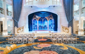 The stage of the Grand Hall set up for a wedding ceremony with chairs and floral arrangements on the Disney Wish
