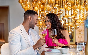 A couple gazing into each other’s eyes and holding glasses of wine while dining at Enchante by Chef Arnaud Lallement
