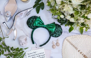 A table with a bouquet, high heels, earrings, a ring in a box, a handwritten note and a Minnie Mouse ear headband