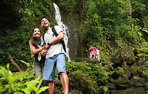 Two couples hiking on a trail next to a waterfall surrounded by lush foliage