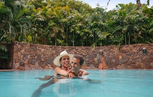 A woman with her arms wrapped around a man from behind as they relax in a pool
