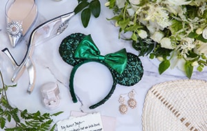 A table with a bouquet, high heels, earrings, a ring in a box, a handwritten note and a Minnie Mouse ear headband